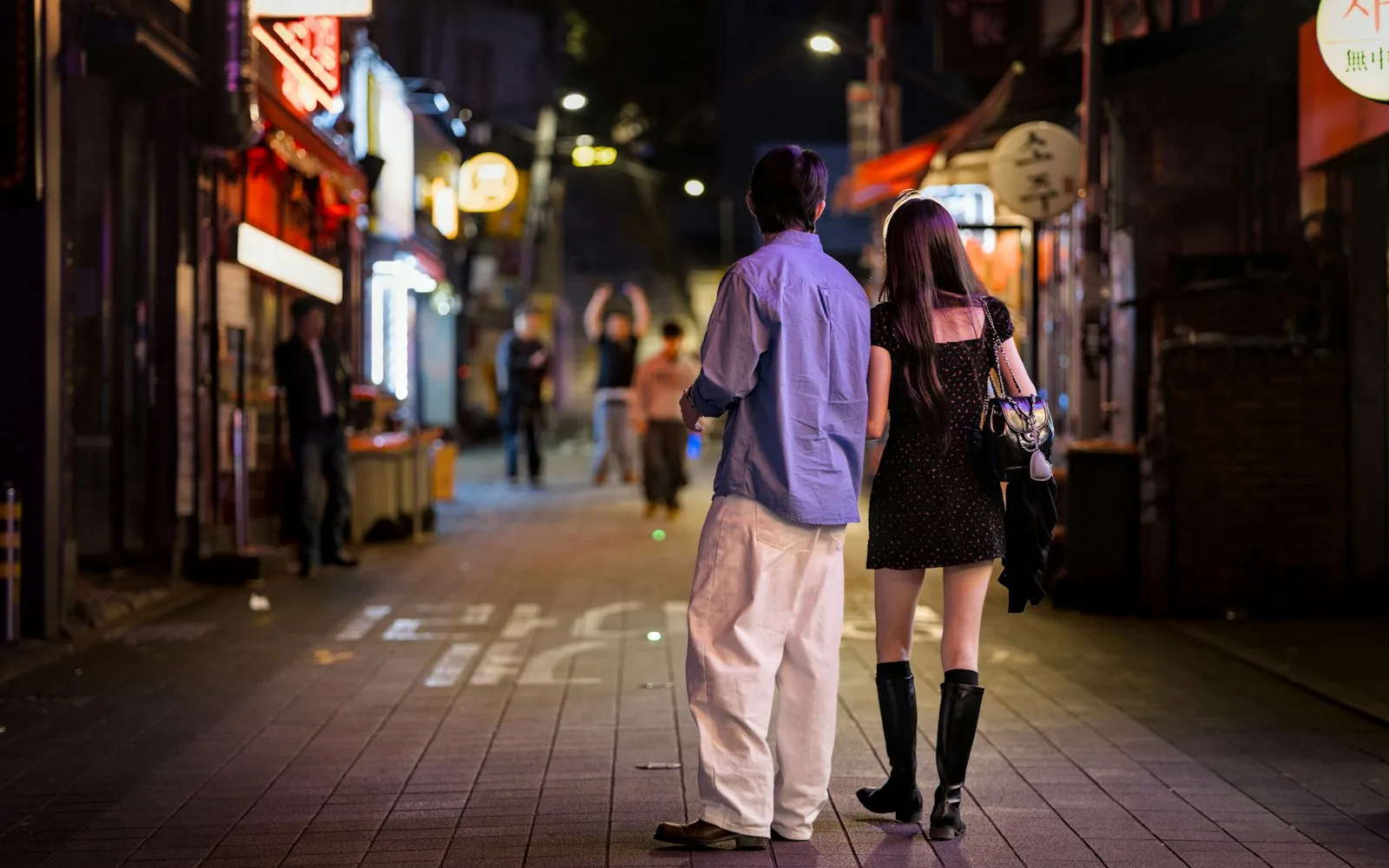 A couple walking down a neon-lit street at night