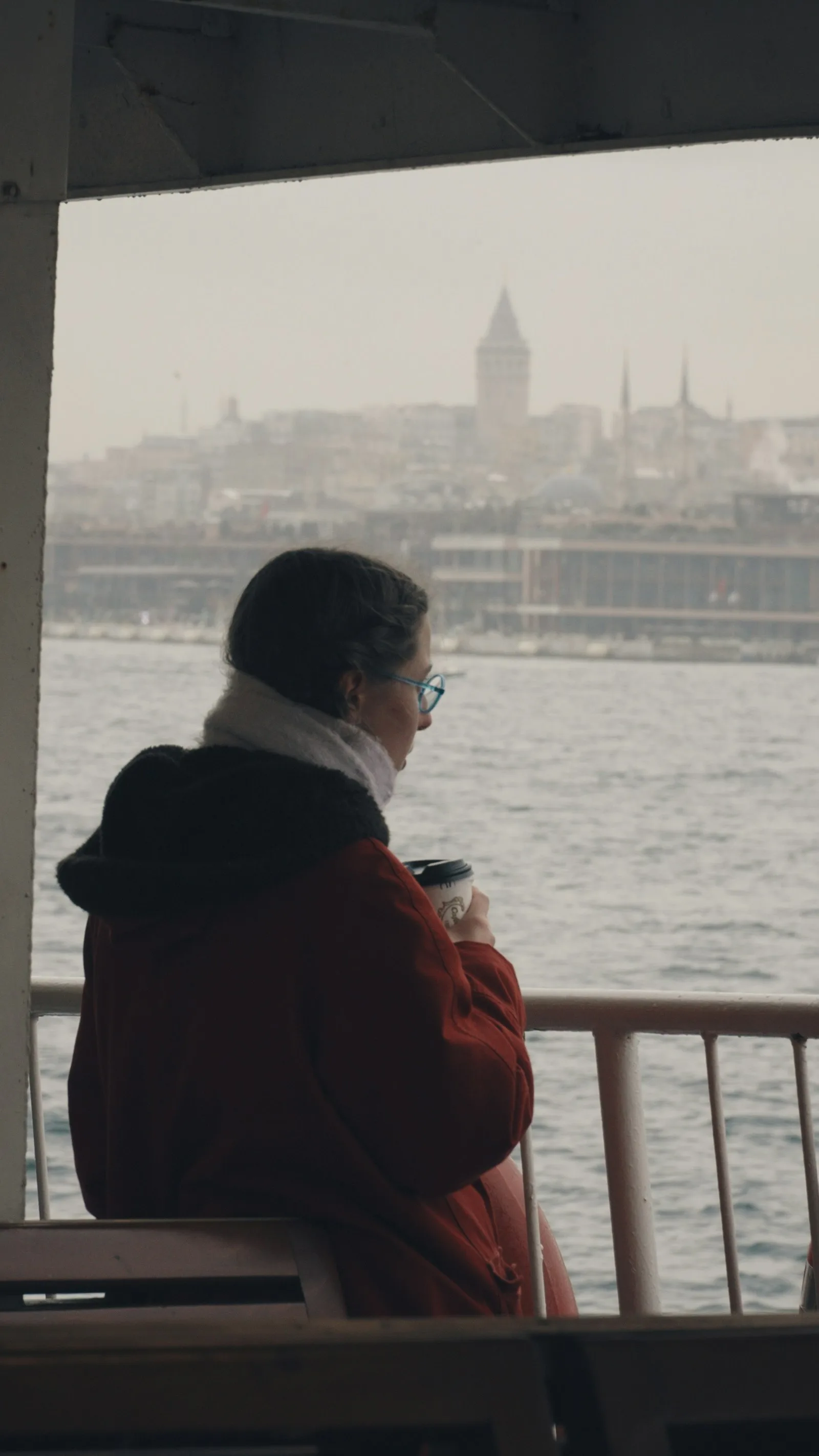 Holding a coffee on the ferry, the city behind